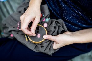 Händer som stoppar ett hål med broderi