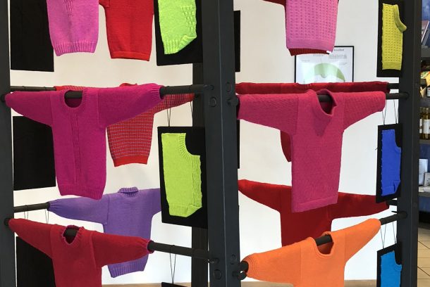 Utställning med stickade tröjor i starka rosa, röda. lila nyanser.