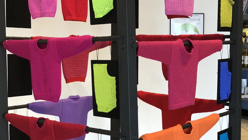 Utställning med stickade tröjor i starka rosa, röda. lila nyanser.