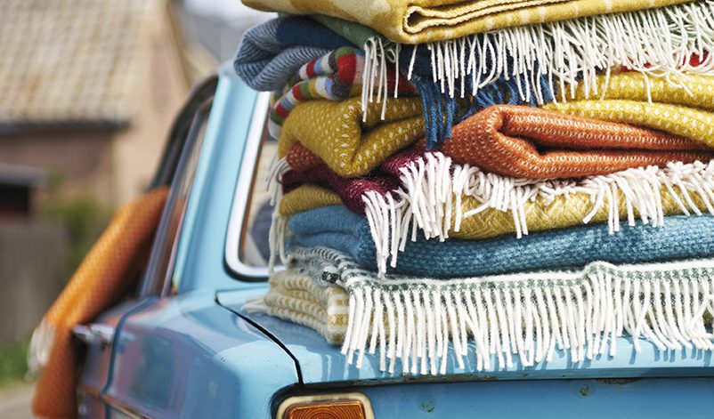 Blå Volvo med en stor hög färgglada filtar ovanpå bakluckan.