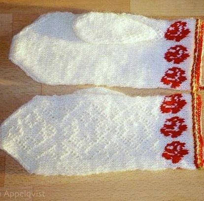 Ett par vita vantar med röda blommor vid handlederna