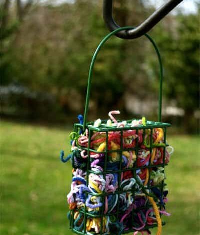 Garnrester i grön metallkorg som hänger på en krok i en grönskande trädgård