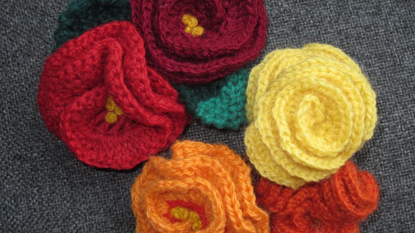Fyra stickade hårspännen i form av röda, orange och gula rosor