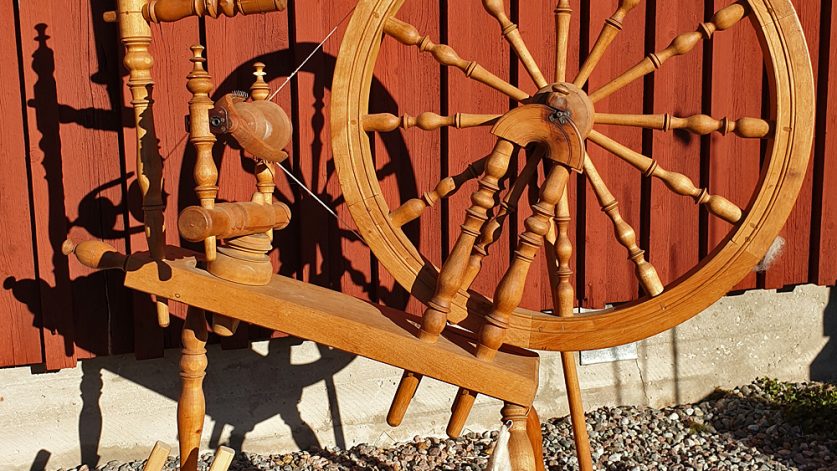 spinnrock och kardor framför en faluröd trävägg