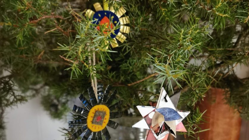 enris i en vas med dekorationer av kapsyler och kläde, samt vikta stjärnor av återbrukspapper