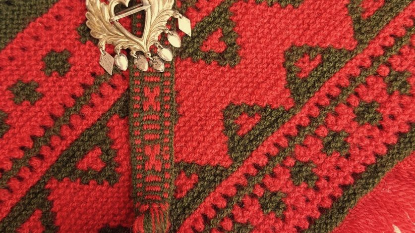 Stickad sjal med vävt band och förgyllt dräktsmycke