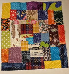 En liten fyrkantig quilt sydd i glada färger