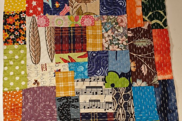 En liten fyrkantig quilt sydd i glada färger