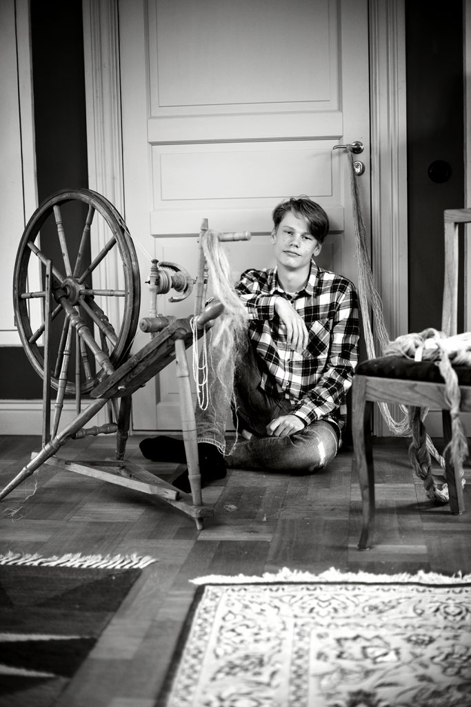 Gustav Karlsryd på golvet med spinnrock framför sig.
