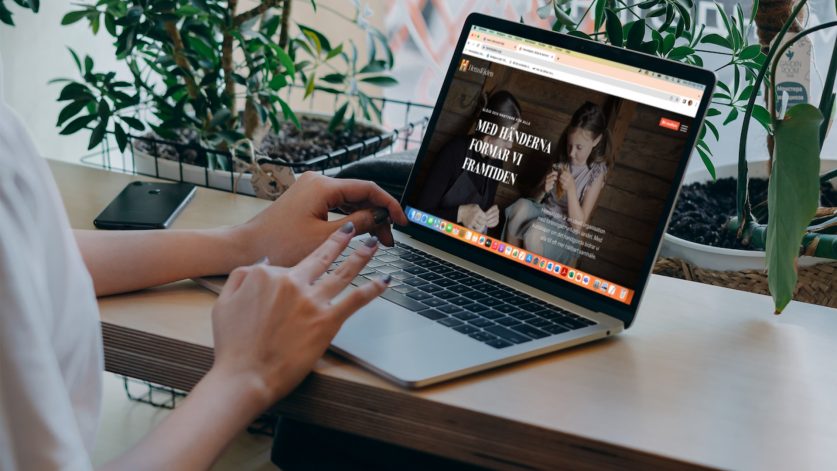 Händer skriver på tangentbordet till bärbar dator som visar startsidan till Hemslöjdens hemsida.