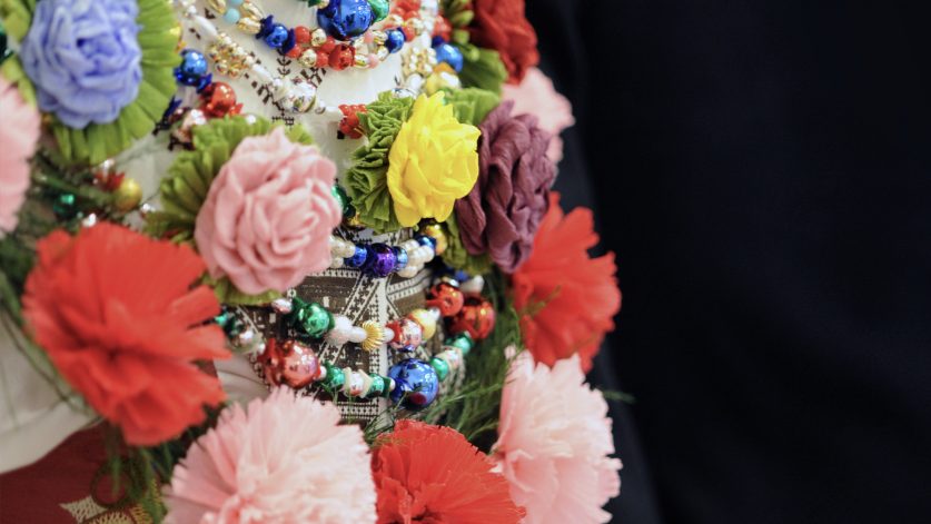 detaljbild på överkropp klädd i livstycke med flera rader halsband av glaspärlor och pappersblommor