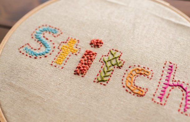 Bokstäverna STITCH broderade på vitt tyg